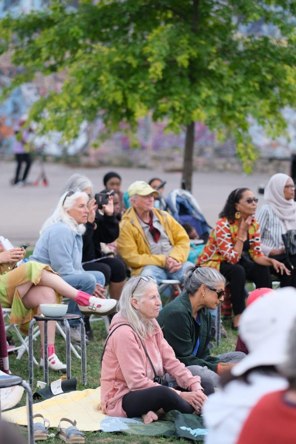 Neighbours seated on chairs and blankets in John Rebecca Park, lending their ears to place-conscious dialogue under a young tree.