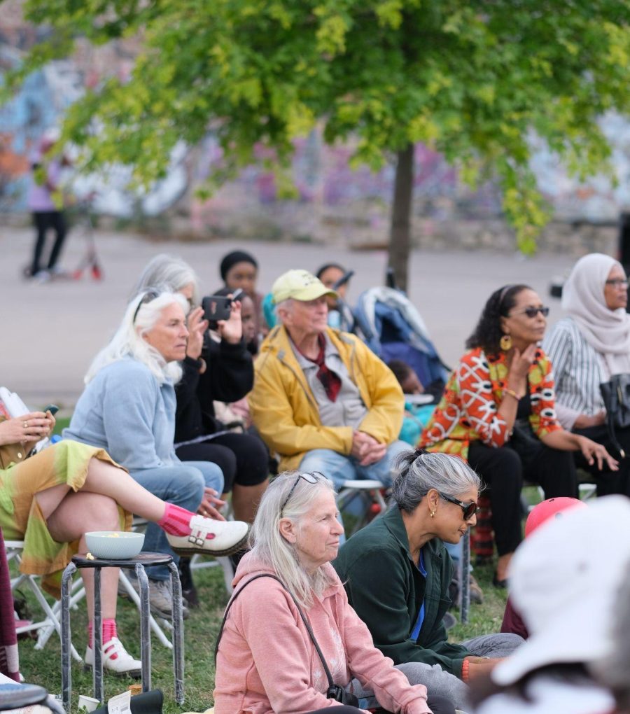 Neighbours seated on chairs and blankets in John Rebecca Park, lending their ears to place-conscious dialogue under a young tree.